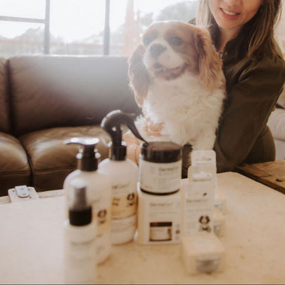 Woman with a dog in a living room surrounded by skincare products