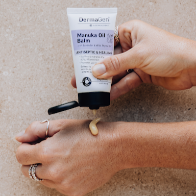 Person applying DermaGen Manuka Oil Balm to their hand on a neutral background